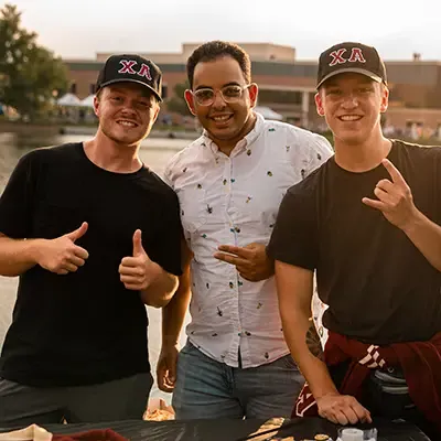 Three Alpha Chi members smiling with thumbs up