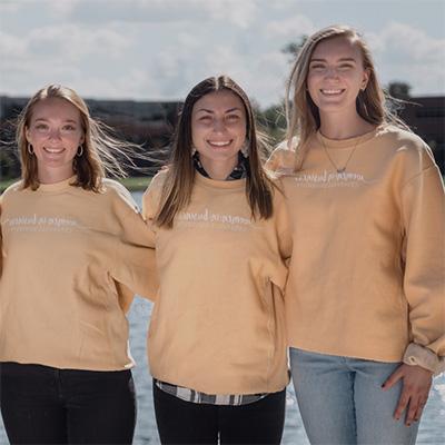 3 college students wearing Women in Business sweatshirts